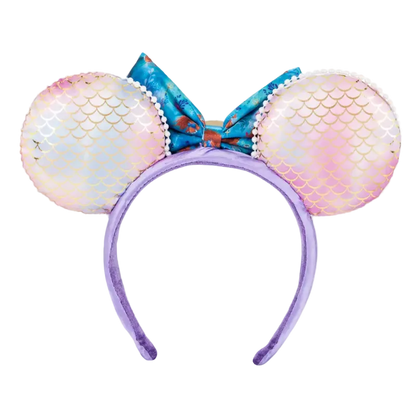 Mermaid-themed mouse ears headband featuring iridescent pink and blue mermaid-scale ears, a blue patterned bow, and a purple headband on a white background.