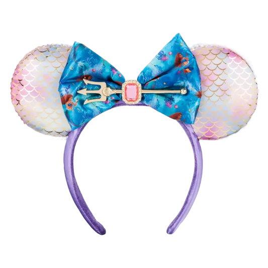 A mermaid-themed mouse ear headband featuring iridescent pink and white mermaid-scale ears, a large blue floral bow with a trident and pink gem accent, and a purple headband.