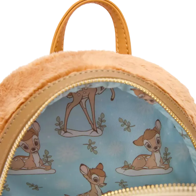 Close-up of a plush mini backpack with a light blue interior printed with Bambi the deer illustrations, tan faux-leather trim and handle, and a gold zipper.