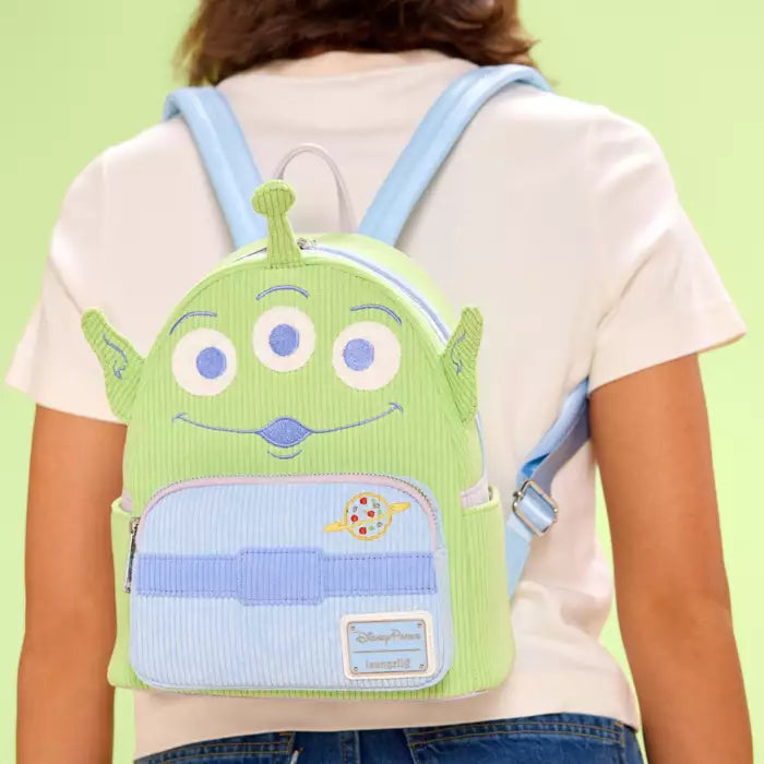 Person wearing a green and blue backpack with a cartoon face design on a light green background