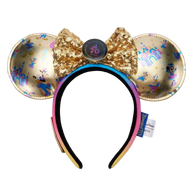 A Disney Minnie Mouse ears headband featuring gold sequined ears with holographic and blue monogram patterns, a large gold sequined bow with a central round button, and a black-to-pink gradient headband.
