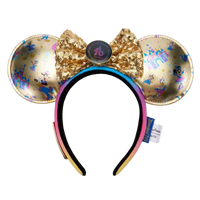 A Disney Minnie Mouse ears headband featuring gold sequined ears with holographic and blue monogram patterns, a large gold sequined bow with a central round button, and a black-to-pink gradient headband.