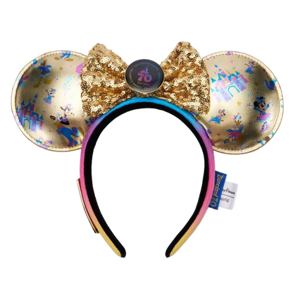 A Disney Minnie Mouse ears headband featuring gold sequined ears with holographic and blue monogram patterns, a large gold sequined bow with a central round button, and a black-to-pink gradient headband.
