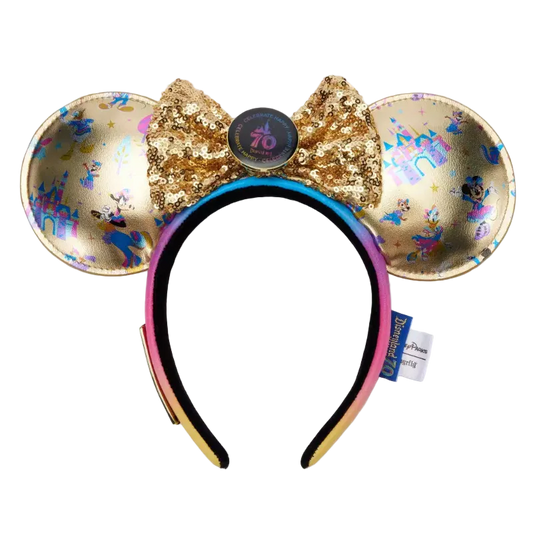A Disney Minnie Mouse ears headband featuring gold sequined ears with holographic and blue monogram patterns, a large gold sequined bow with a central round button, and a black-to-pink gradient headband.