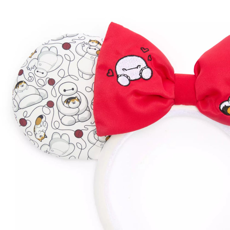 A close-up of a Disney Minnie Mouse-inspired headband featuring a large red bow with an embroidered cartoon character and a white ear cup covered in a gray cartoon print.