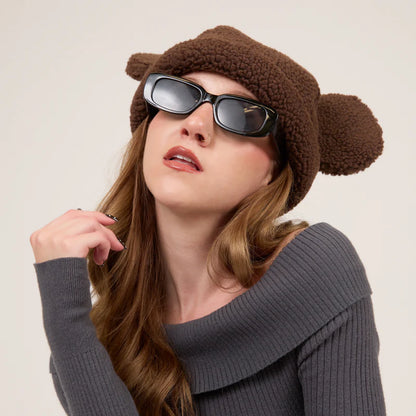 Woman wearing a brown knit hat with ears and dark sunglasses against a plain background
