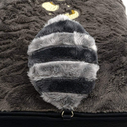 Close-up of a fluffy, gray and black bee-shaped pillow on a textured surface.