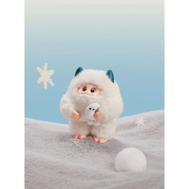 Plush toy resembling a fluffy creature with blue horns on a textured surface with a star decoration.