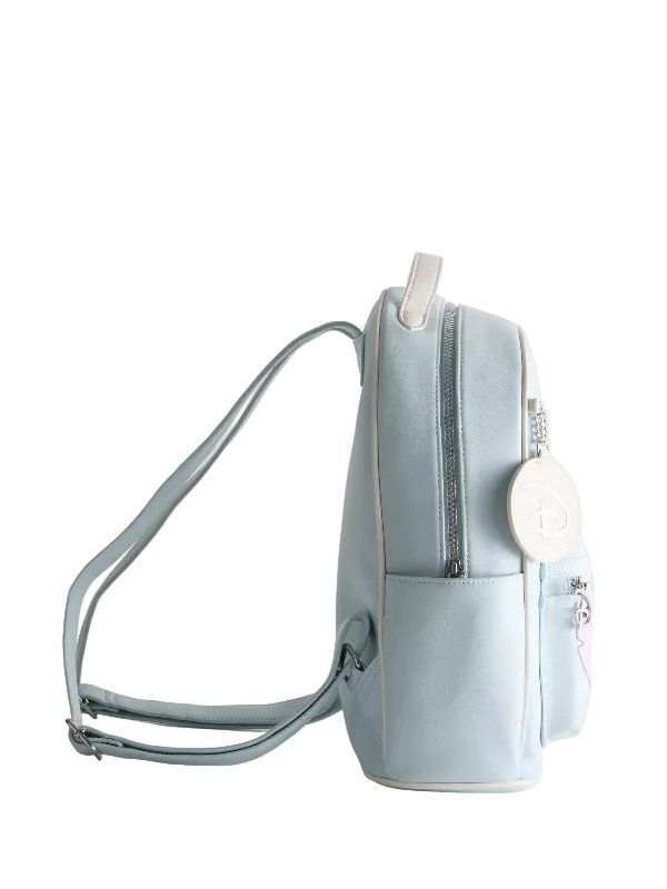 A light blue faux-leather backpack with a front pocket, silver zippers, and a white circular charm featuring a monogram logo, shown against a plain light gray background.