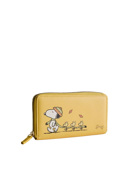 A yellow zip-around wallet featuring a printed cartoon illustration of Snoopy and the Beagle dogs walking under falling leaves, shown on a light gray background.