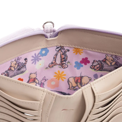 Close-up of a beige tote bag interior showing a light purple zipper and a pink fabric lining printed with Winnie the Pooh, Tigger, and other cartoon characters with colorful flowers.