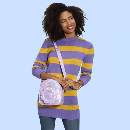Woman wearing a purple and yellow striped sweater holding a pink crossbody bag against a light blue background