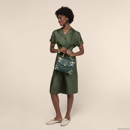 Woman holding a green handbag wearing a matching outfit against a beige background