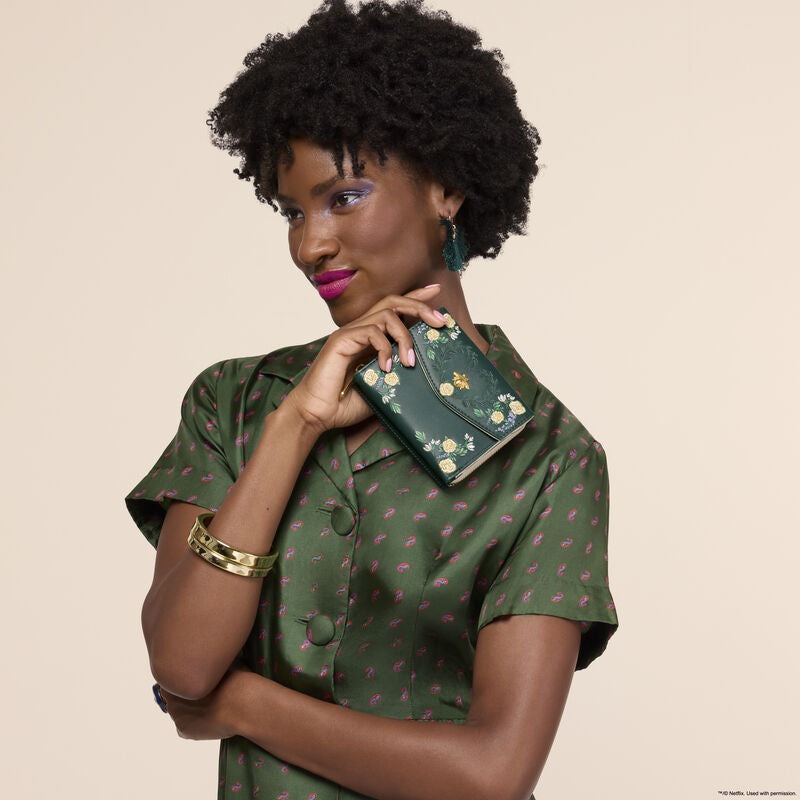 Woman holding a green floral clutch against a beige background