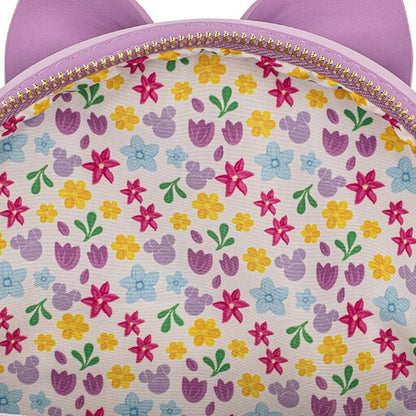 Close-up of a pastel floral patterned fabric with purple cat-ear shapes along the top edge and a gold zipper.