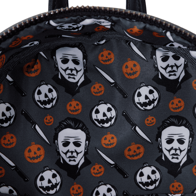 Backpack with Halloween-themed design featuring Michael Myers, pumpkins, and knives on a dark background.
