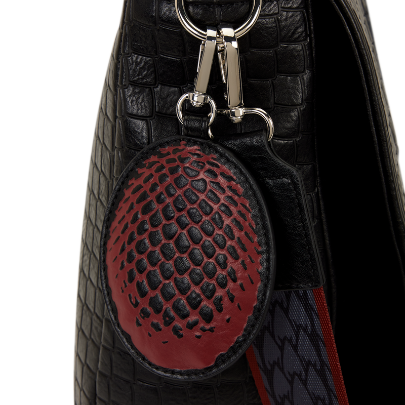 Black textured bag with a red and black patterned keychain on a white background