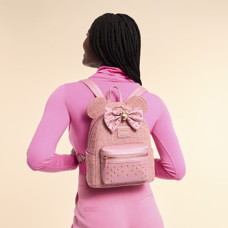 Person wearing a pink backpack with a bow and gold accents on a beige background