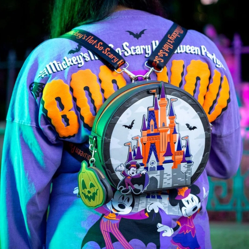 Person wearing a colorful jacket with 'Mickey's Not-So-Scary Halloween Party' text, holding a themed bag with castle design.