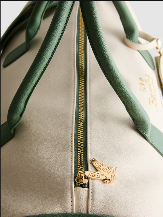 Close-up of a beige handbag with green accents and a gold zipper and clasp.