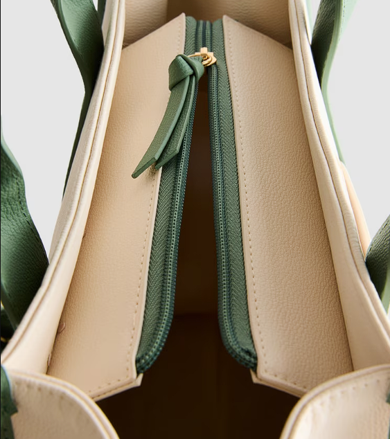 Close-up of a beige handbag with green zipper and handle