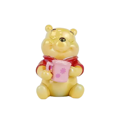 A small Winnie the Pooh bear figurine holding a pink mug with pink flower details, set against a plain white background.