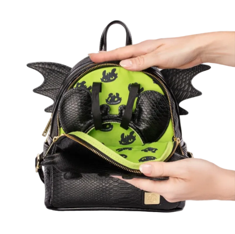 A black dragon-themed backpack with a textured python-skin style exterior, gold zippers, and wing-like side details, shown open with hands holding it to reveal a bright lime green interior lined with black dragon silhouettes.