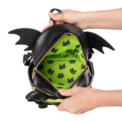 A black dragon-themed backpack with textured faux-leather finish, gold zippers, and a bright green interior patterned with small black dragon silhouettes. Hands are shown holding the open bag against a white background.