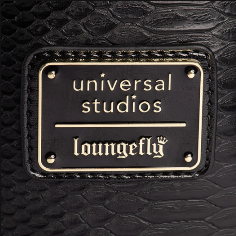 Close-up of a black crocodile-embossed leather surface with a rectangular black metal plaque featuring gold lettering that reads 'universal studios' and 'loungefly'.