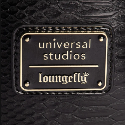 Close-up of a black crocodile-embossed leather surface with a rectangular black metal plaque featuring gold lettering that reads 'universal studios' and 'loungefly'.