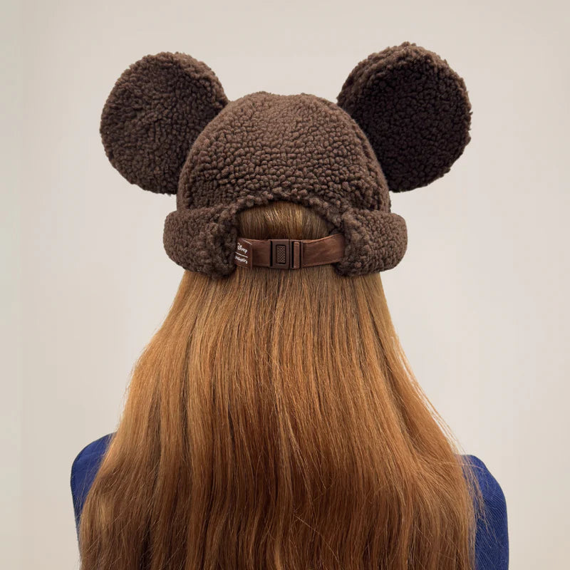 Brown fleece hat with mouse ears worn by a person with long hair on a plain background