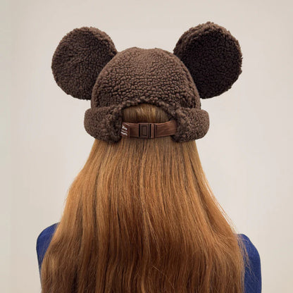 Brown fleece hat with mouse ears worn by a person with long hair on a plain background