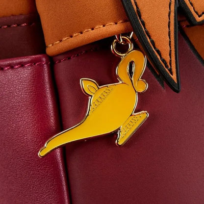 A close-up of a metallic gold Aladdin lamp-shaped charm hanging from a brown leather strap against a burgundy leather background.