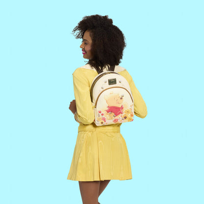 Woman wearing a yellow dress with a Winnie the Pooh backpack on a solid blue background