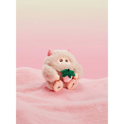 Plush toy resembling a monkey holding a green leaf on a pink background