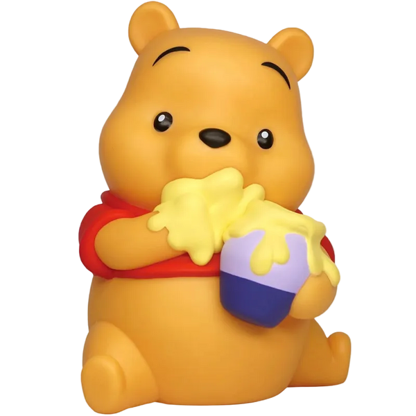 A Winnie the Pooh bear figurine or bath toy in a sitting pose, holding a honey pot with yellow honey dripping over it. The bear is yellow with a red shirt, and the pot is purple and blue, set against a plain white background.