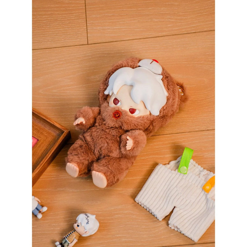 Plush toy resembling a bear in a brown outfit on a wooden floor with a white towel and green item.