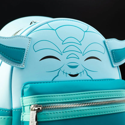 A close-up of a light blue and turquoise character backpack featuring a smiling winking face design on the front, with ear-like side panels and a silver zipper.