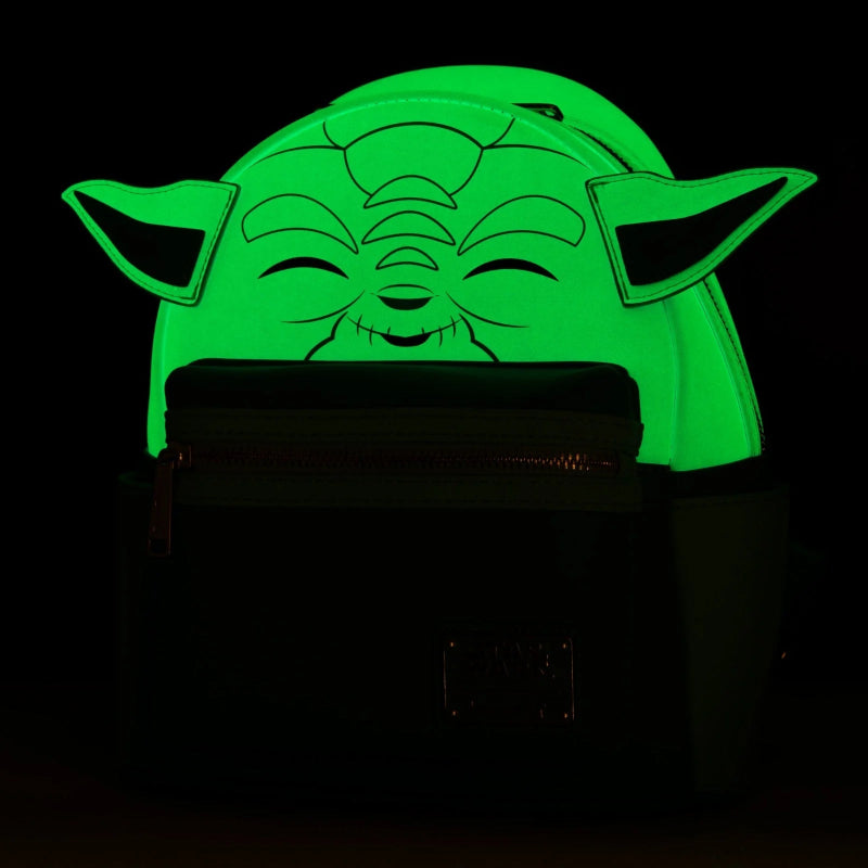 A black backpack featuring a glowing green Yoda face graphic on the back, photographed in a dark environment to highlight the luminescent effect.