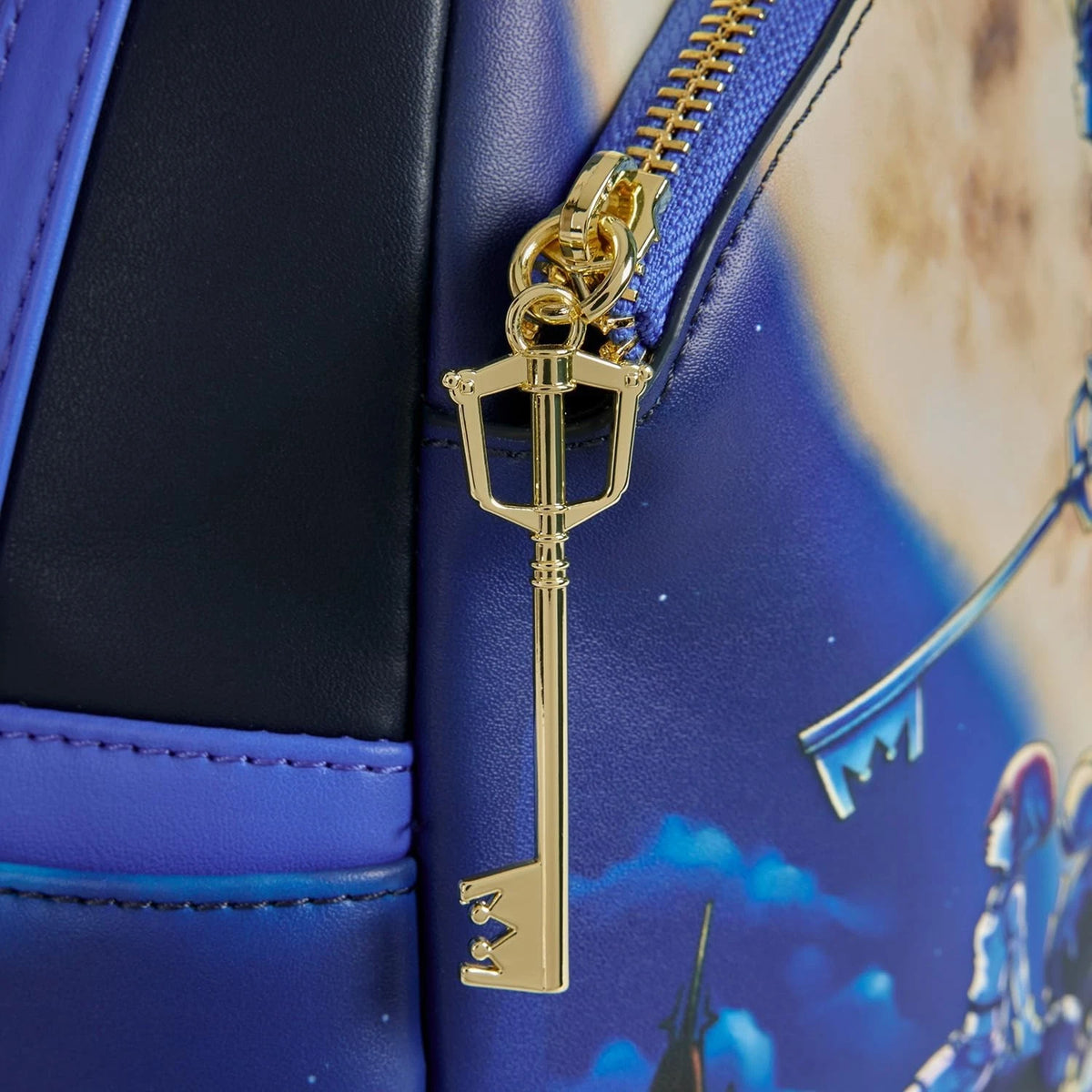 Gold key-shaped zipper pull on a blue bag with a castle design.