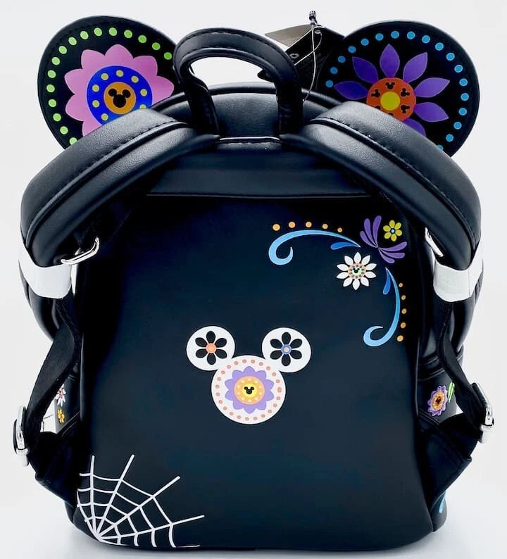 A black backpack styled like a Mickey Mouse ear backpack, decorated with colorful Dia de los Muertos-style floral patterns on the ears, a floral mouse face on the front, and a white spiderweb print in the bottom left corner.