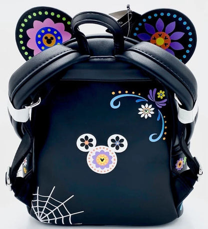 A black backpack styled like a Mickey Mouse ear backpack, decorated with colorful Dia de los Muertos-style floral patterns on the ears, a floral mouse face on the front, and a white spiderweb print in the bottom left corner.