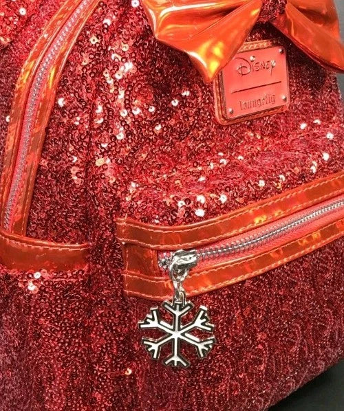Close-up of a red sequined Disney Loungefly bag with a metallic copper bow, silver zipper, and a silver snowflake charm.