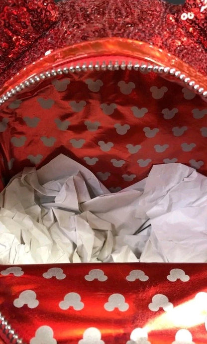 Close-up of the inside of a red sequined bag or pouch, showing a silver zipper trim and a red lining patterned with silver Mickey Mouse head silhouettes. White tissue paper is visible inside.