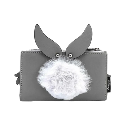 A gray zip-around wallet featuring a rabbit face design with upright ears, silver metal eye studs, and a fluffy white faux-fur pom-pom in front. A small black fabric tag with white text is visible on the right side.