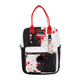 A small tote bag with a black and white split design, red handles, and red blood-splatter print. It features a front zippered pocket with a black skull patch, a hanging character charm, and a brand patch that reads 'Mortuary'.